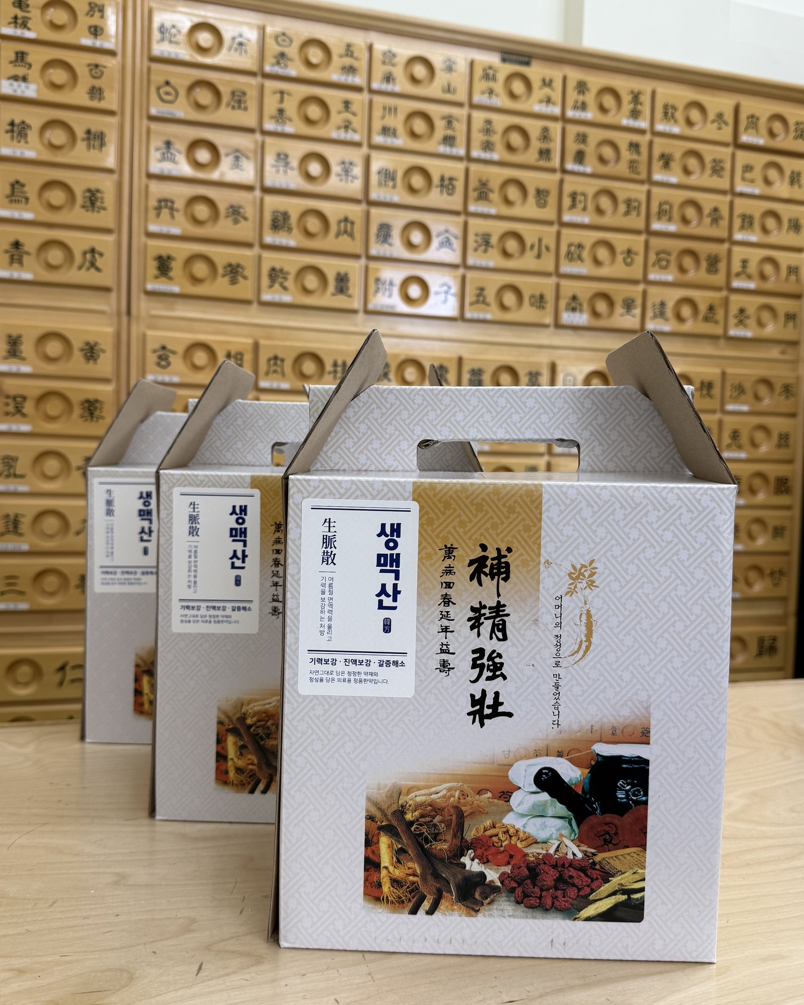 Stack of premium ginseng-based 보정강림 (saengmaeksan) gift boxes against the apothecary cabinet